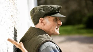 Older veteran in a flat cap and vest looking out a window