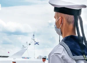 Asbestos Exposure in U.S. Navy Shipyards: The Hidden Risk Still Affecting Veterans 1 oung U.S. Navy sailor in full dress uniform wearing a protective medical mask, representing asbestos exposure risks in shipyards
