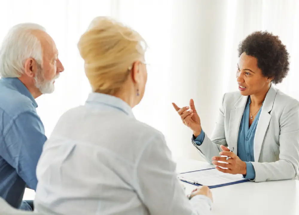A lawyer explaining legal settlement options and veterans' benefits to an elderly couple in a bright office.