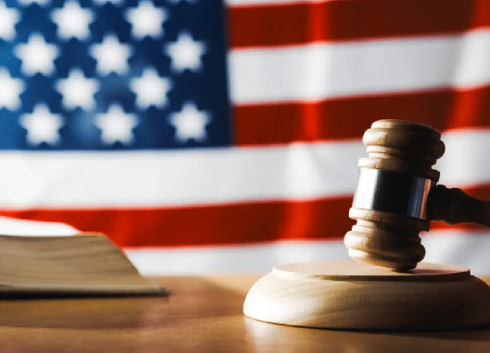 A wooden gavel resting on a wooden table and a flag of united states, symbolizing legal jurisdiction and venue selection.