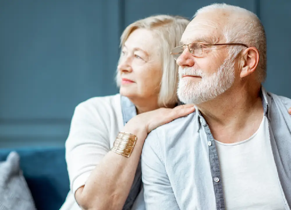 A senior man and woman looking thoughtfully into the distance, representing the emotional journey of families facing a mesothelioma diagnosis.