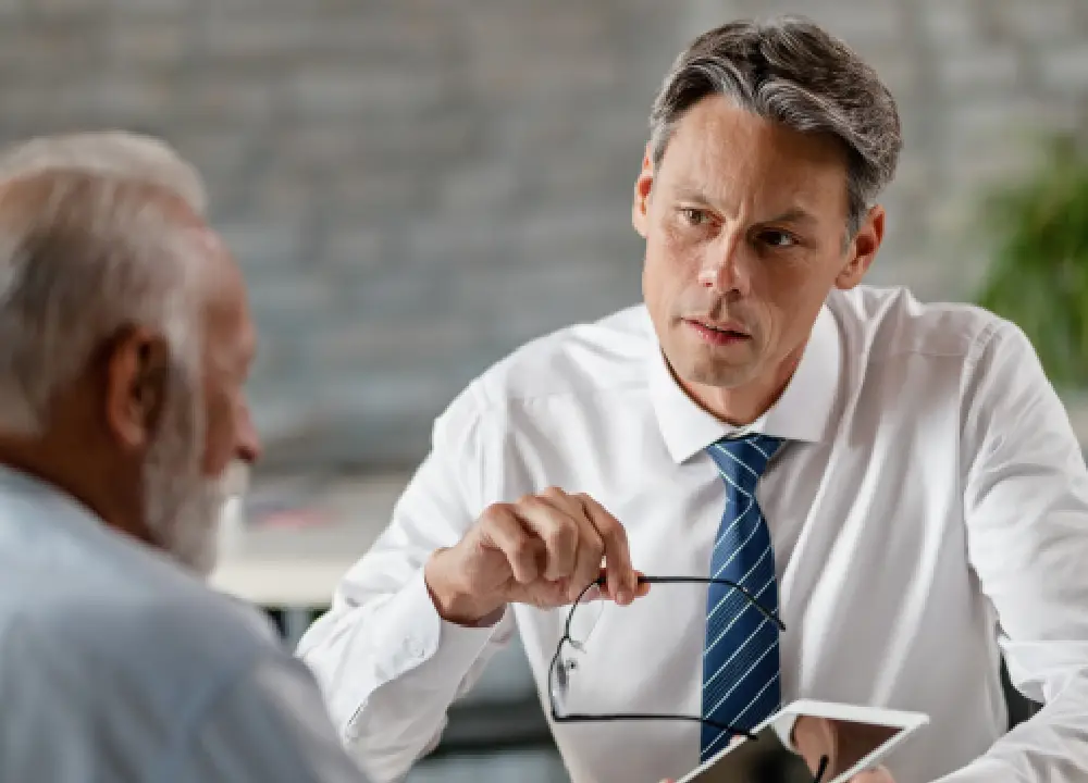 An experienced lawyer talking supportively with a senior man in a professional law office.