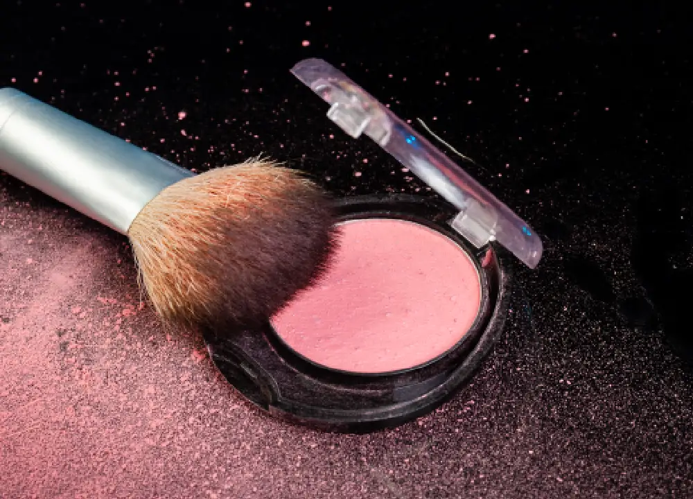Close-up of a makeup brush next to a round cosmetic powder container.