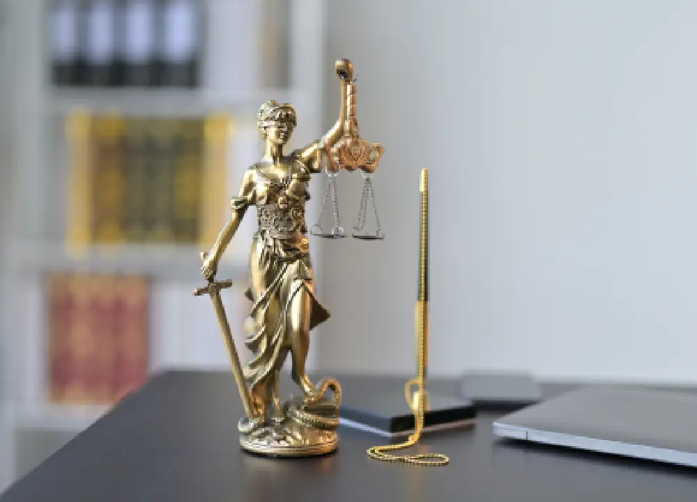 A close-up of the Lady Justice statue on a wooden desk, symbolizing legal rights and protection.
