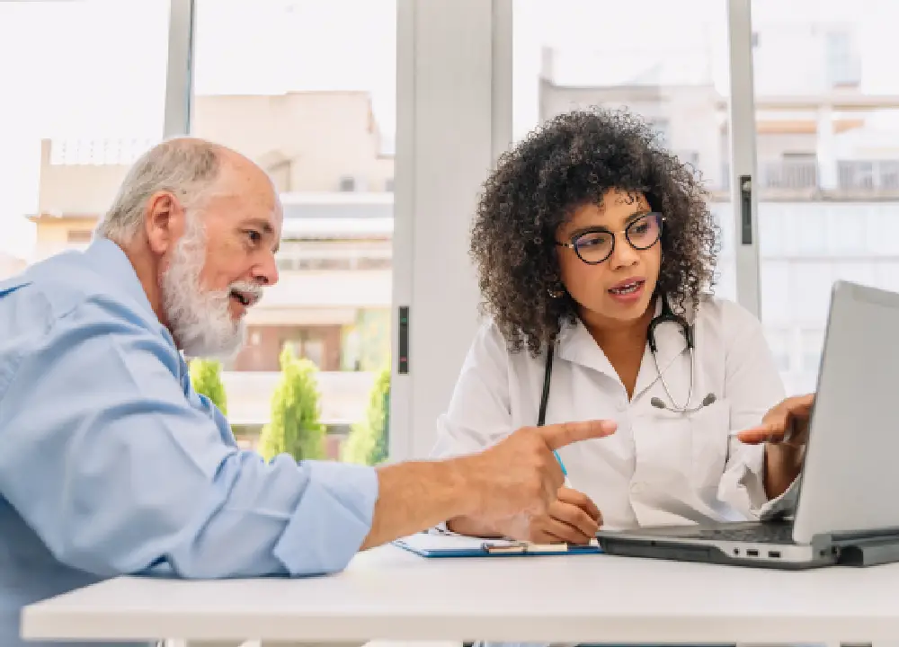 A doctor showing a senior patient medical information on a laptop screen in a clinic.