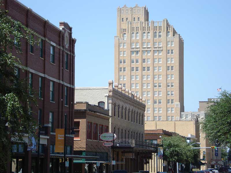 Historic brick buildings and a tall tan high-rise along a downtown street in Abilene, Texas